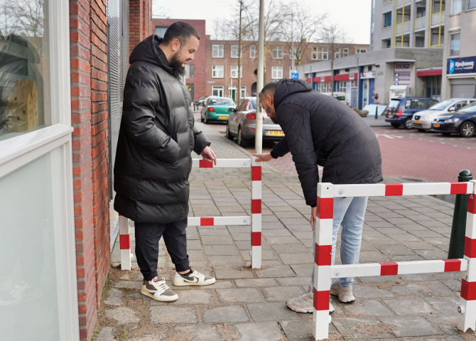Twee mannen op straat aan het kijken naar een rood met wit hekje.
