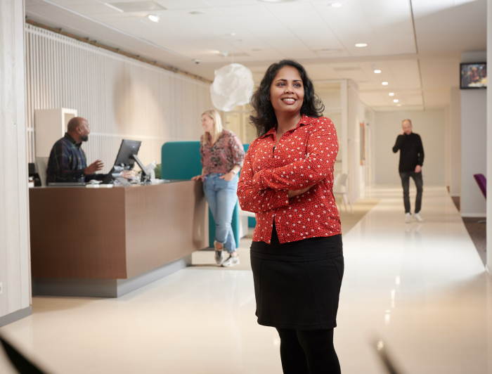 Collega van Staedion poseert bij de receptie van Staedion. Baliemedewerker is op de achtegrond in gesprek