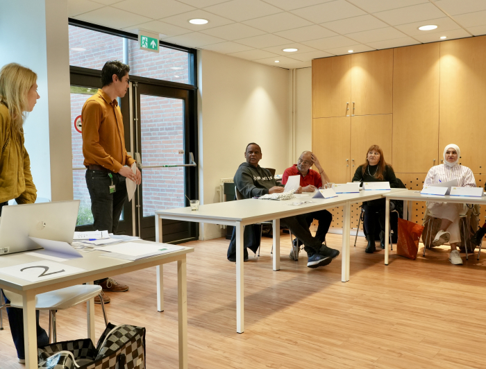 workshopleider Carin geeft workshop en staat voor een aantal bezoekers die aan tafel zitten