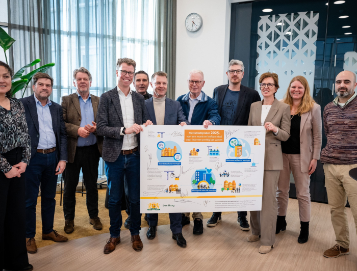 Groepsfoto van Martijn Balster en Gijsbert van Herk met een bord van de prestatieafspraken in handen met daarom heen alle woonpartners 