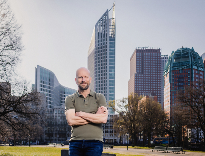 Projectmanager leefomgeving Stephan staat met armen over elkaar en kijkt in de camera. Op de achtergrond de skyline van Den Haag.