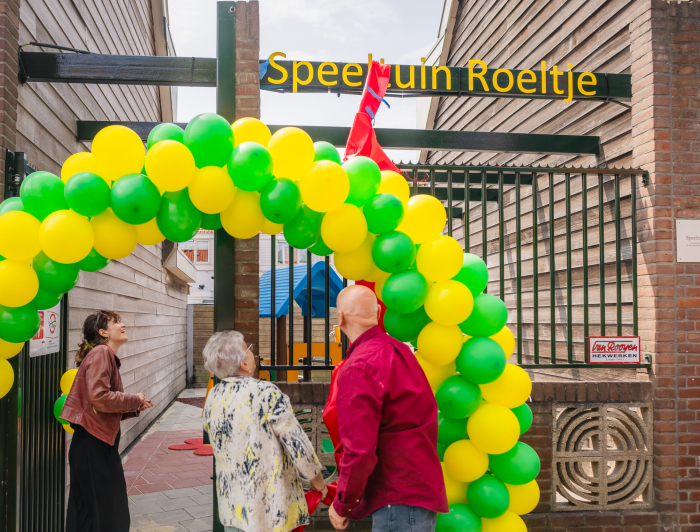 Twee dames en meneer onder een boog ballonnen en onthullen bord met naam Speeltuin Roeltje