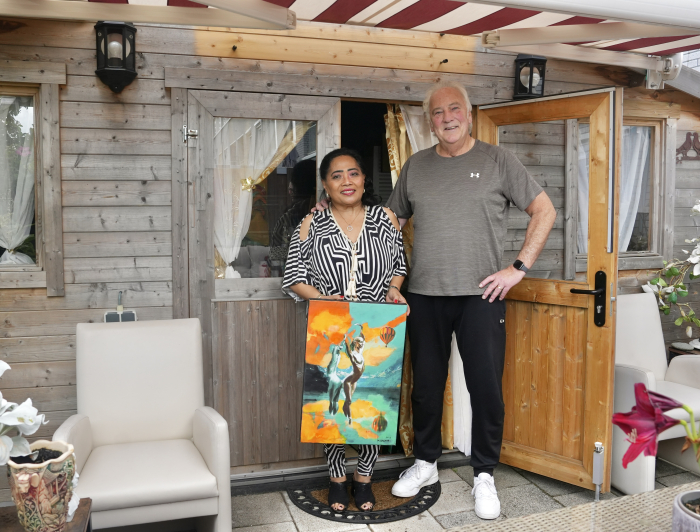 Een meneer en mevrouw poseren voor hun huis met een schilderij in de handen
