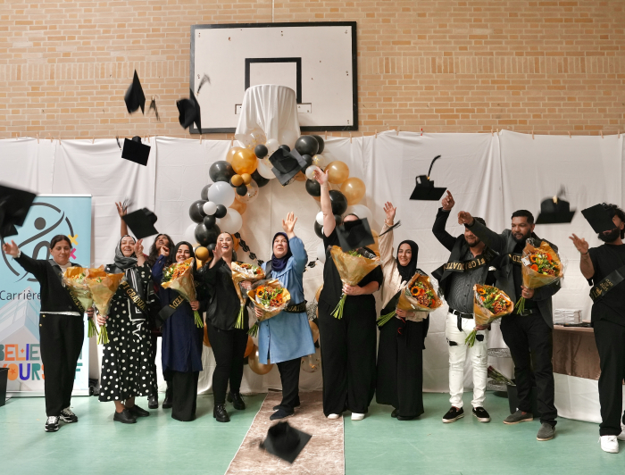 Een groep dames en heren gooien hun geslaagd hoedje in de lucht, ook houden ze bloemen vast