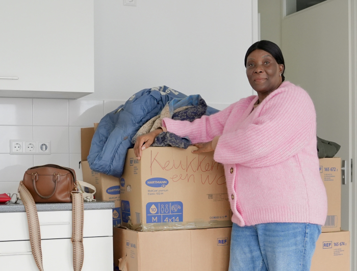 Mevrouw de Lannoy in haar nieuwe huis. Ze staat voor een stapel verhuisdozen.